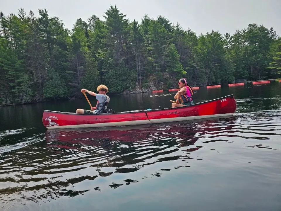 Two Scouts paddling a red canoe past a pine forest in Algonquin Provincial Park