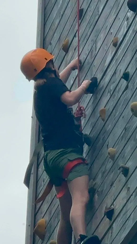A Scout in a helmet and harness climbs the camp climbing wall
