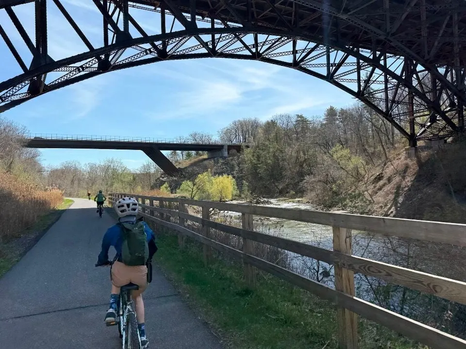 Cyclists on the rail trail beneath a tall steel bridge