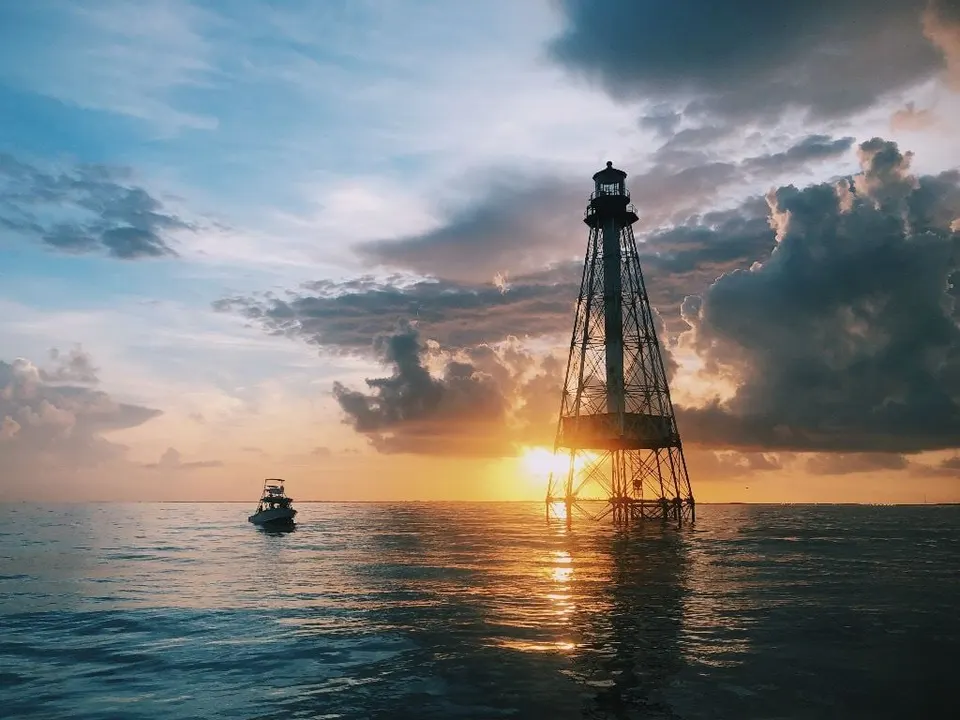 A reef lighthouse at sunset with a boat passing by
