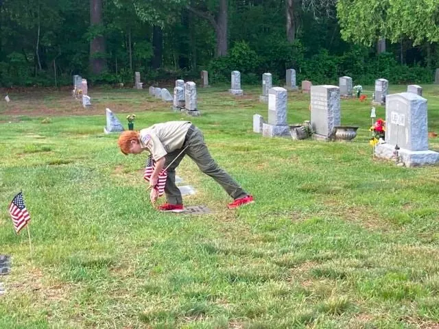 A Scout places an American flag at a veteran's grave before Memorial Day