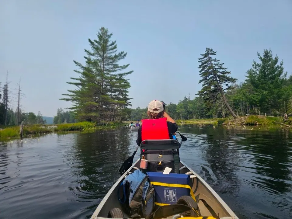 A Scout in a red life jacket paddles from the bow of a canoe through a quiet channel