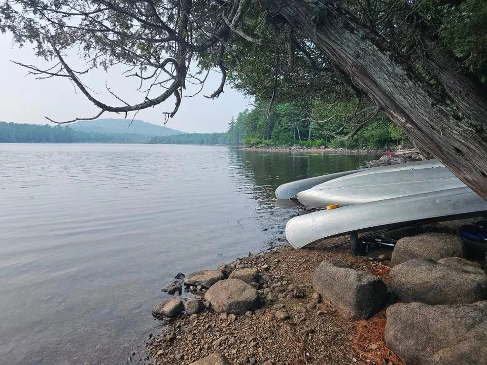 Aluminum canoes pulled up on a rocky shore beside a calm lake