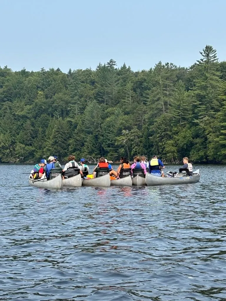 Canoes rafted together in the middle of a lake, surrounded by forest