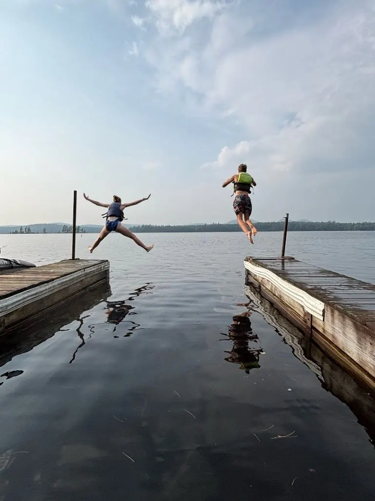Two Scouts leap off the ends of a dock into a still lake