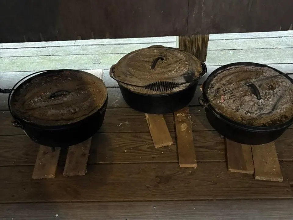 Three Dutch ovens lined up on a log, ready for a cooking competition